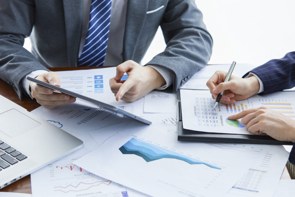 A man pointing his hands towards his tablet and explaining something to his co-worker.