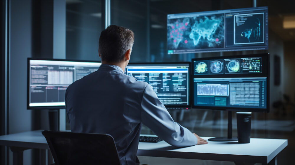 A man working in front many PC's sitting on a chair.