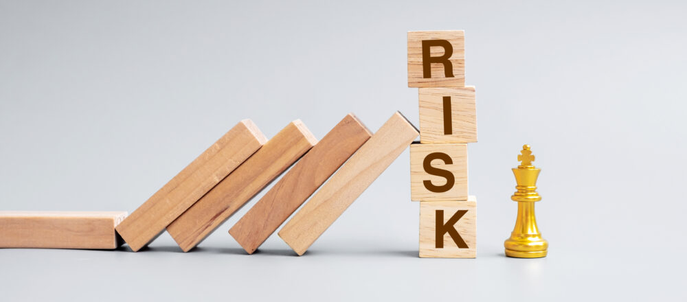 A row of wooden blocks stacked on top of each other, with the word "RISK" spelled vertically on the top three blocks.