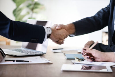 Business people shaking hands together with laptop and notes on the table.