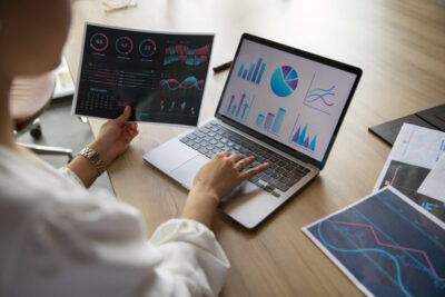 A business woman entering data in the laptop in right hand, by holding a chart in her left hand.